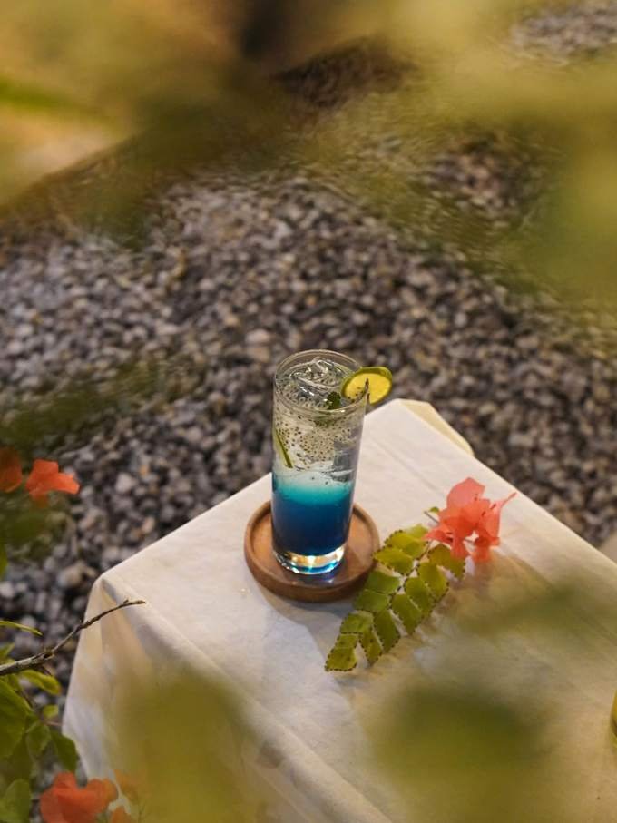 A blue soda on a white table with bougainvillea flowers
